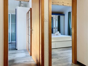 A bedroom with a bed, a wooden wardrobe, and a view through an open door.