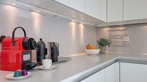 Una cocina moderna con una cafetera expreso roja, dos tazas y un cuenco con fruta.