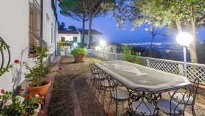 Une terrasse avec une table et des chaises, un pot de fleurs et une vue sur le paysage urbain au crépuscule.