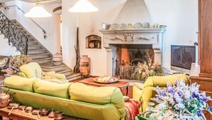 Un salon avec une cheminée, des canapés verts, une table en bois avec du matériel de cuisine et un escalier.