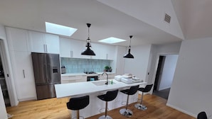 Una cocina moderna con una isla central, taburetes de bar, un refrigerador de acero inoxidable y tragaluces.