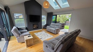 Una sala de estar moderna con un televisor de pantalla plana, sofás grises, chimenea y ventanas amplias.