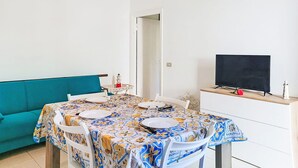 En matplats med ett bord dukat för fyra personer, en tv på ett träskåp och en turkosfärgad soffa.