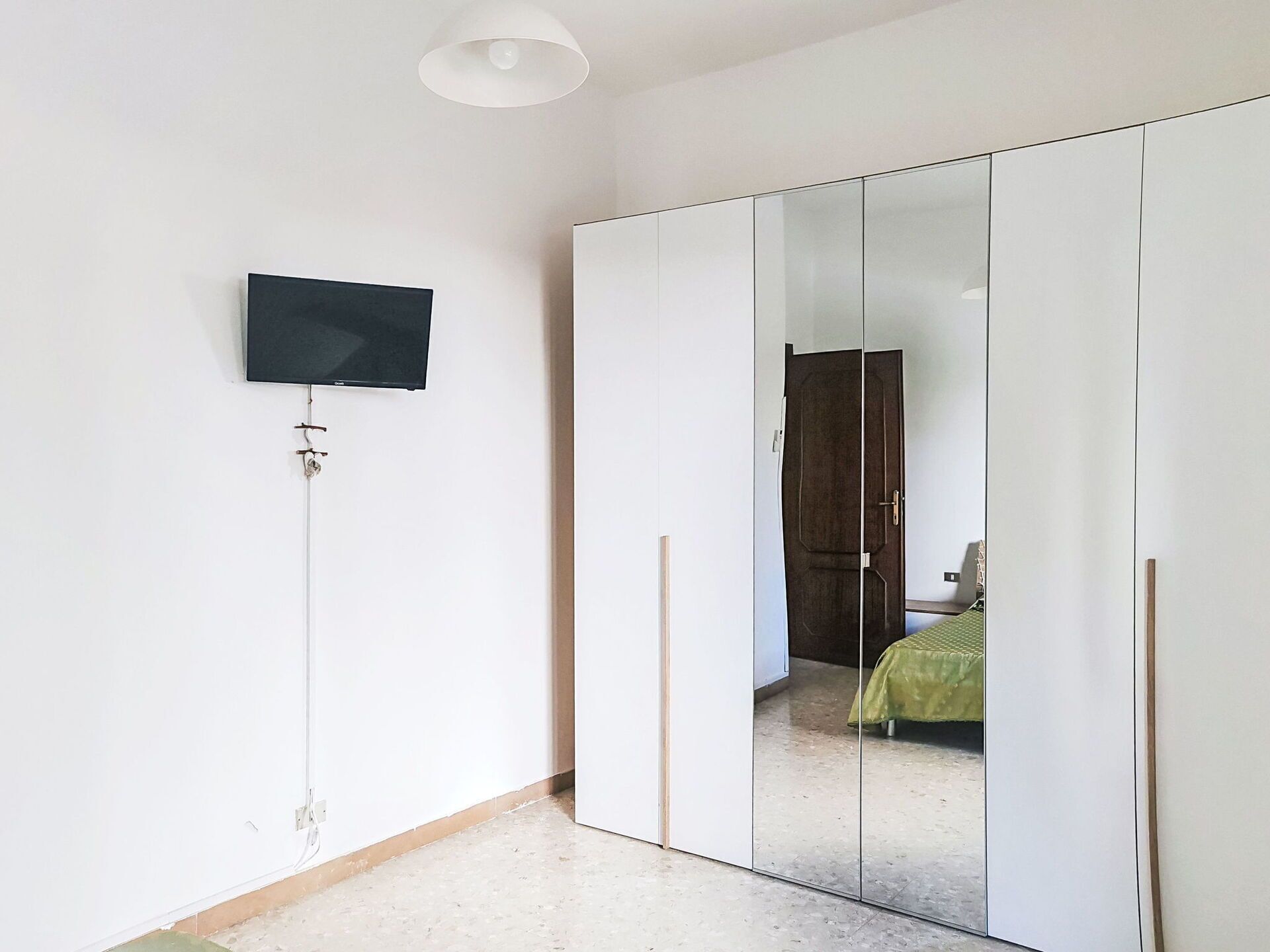 Een kamer met een aan de muur bevestigde televisie, een garderobe met spiegeldeuren en een bed met een groene plaid.