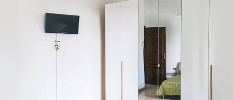 Een kamer met een aan de muur bevestigde televisie, een garderobe met spiegeldeuren en een bed met een groene plaid.