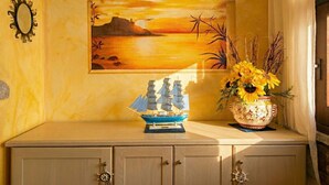 Eine Wand mit einem Gemälde von einem Sonnenuntergang über Wasser, einem dekorativen Schiffmodell und einer Vase mit Sonnenblumen.