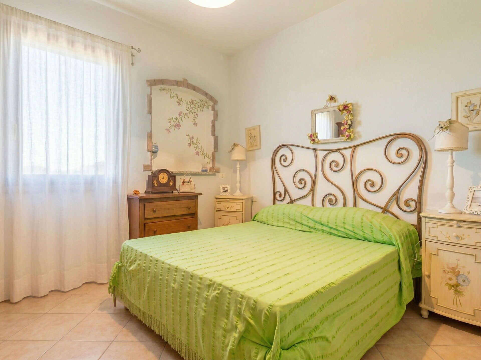 A bedroom with a bed, a dresser, a nightstand, a mirror, and a window with curtains.