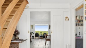 A room with a wooden staircase, a desk with a vase, a chair, and a view of the outdoors.