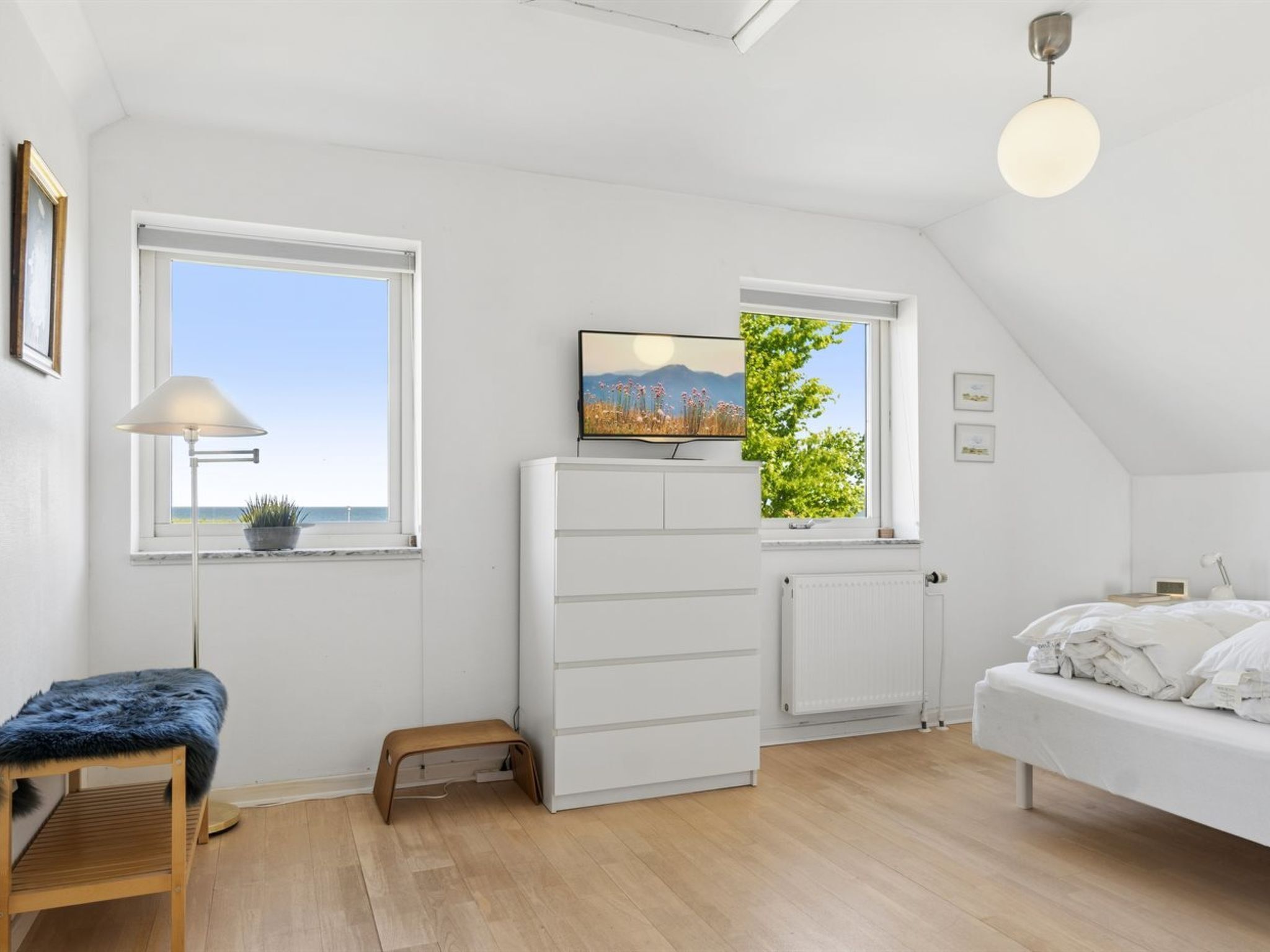 An attic bedroom with a bed, a desk with a chair, a radiator, and a TV on a shelf.