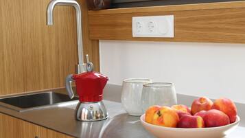 A kitchen with a stainless steel sink, a red coffee maker, a bowl of fruit, and two ceramic cups.