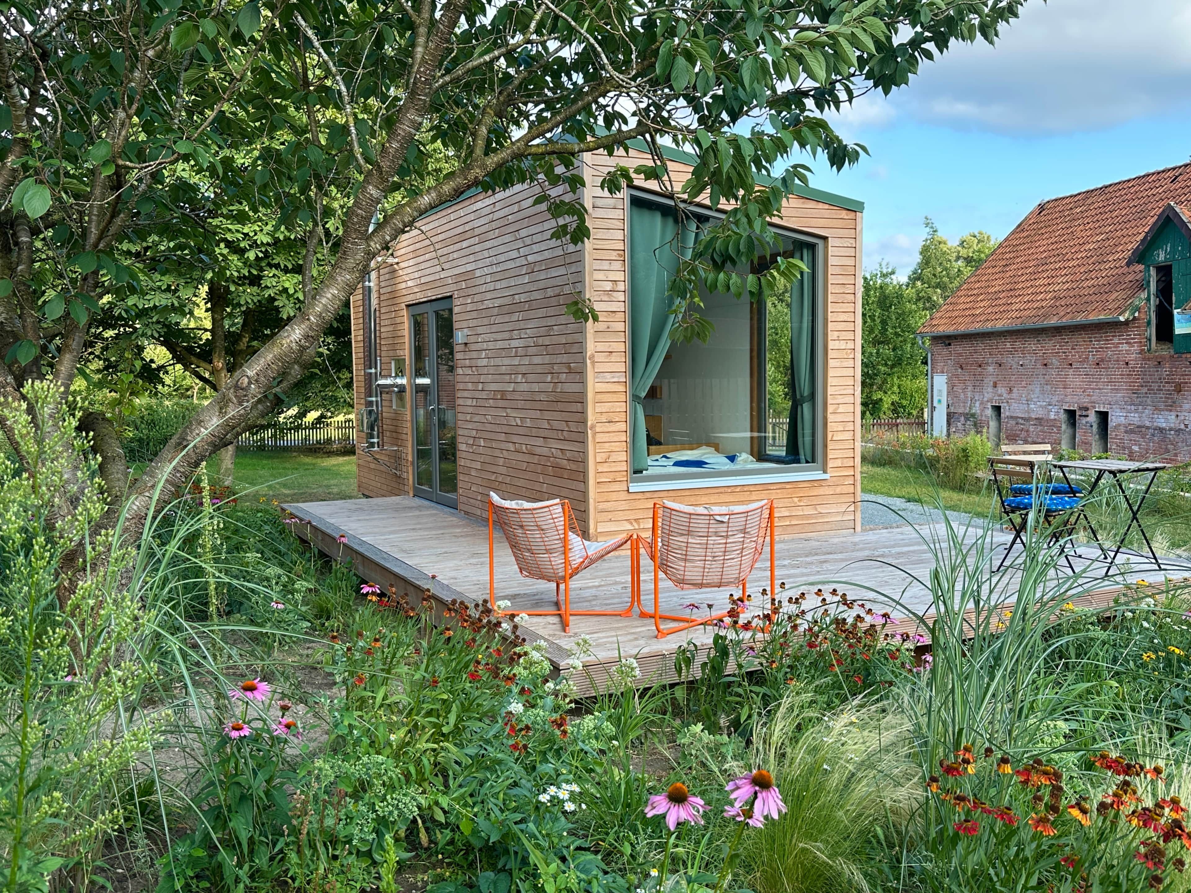 A modern wooden cabin with a glass door, a small deck, and a chair.