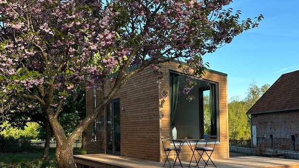 Uma cabana moderna de madeira com porta de vidro, um deck e uma mesa com cadeiras.