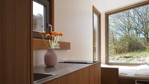 Uma cozinha moderna com bancada de madeira, um vaso rosa com flores e uma janela com vista para árvores.
