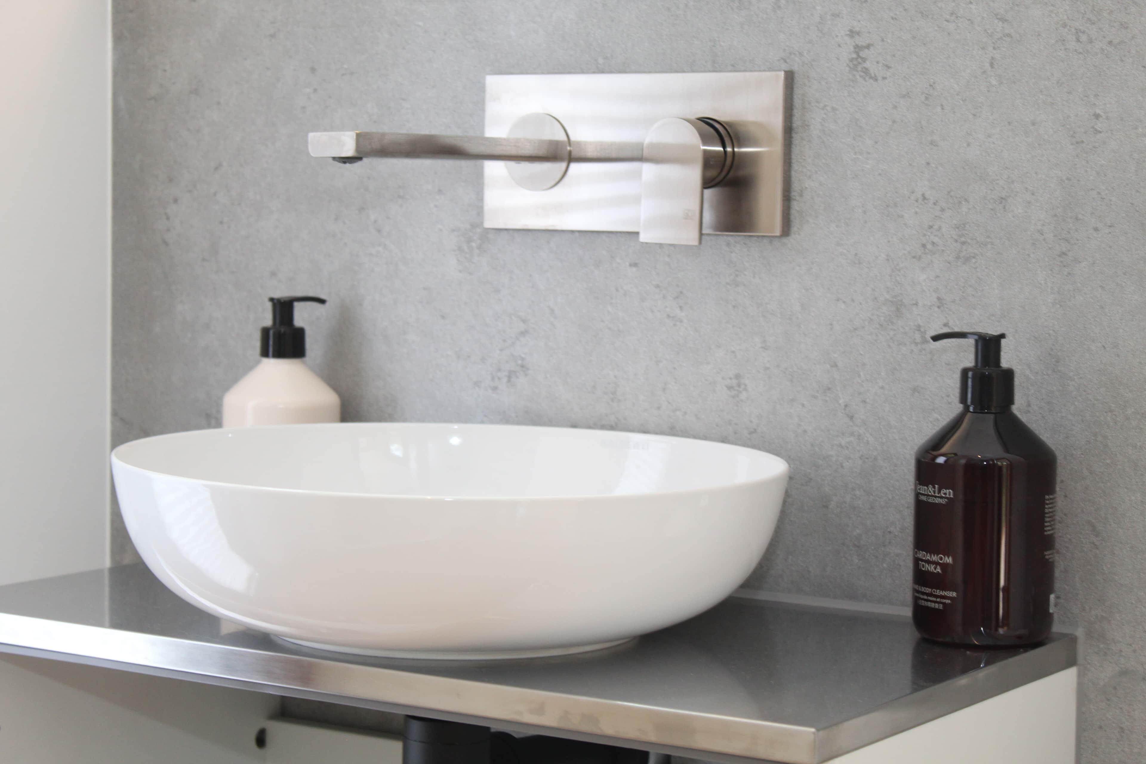 Un baño con un lavamanos blanco de diseño, un grifo moderno y una botella de jabón en la encimera.
