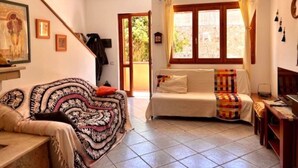 A room with a sofa, a bed, a window with curtains, a wall-mounted air conditioner, and a tiled floor. - Beautiful private villa for 5 people with WIFI, A/C, TV, terrace and panoramic view (Villasimius)