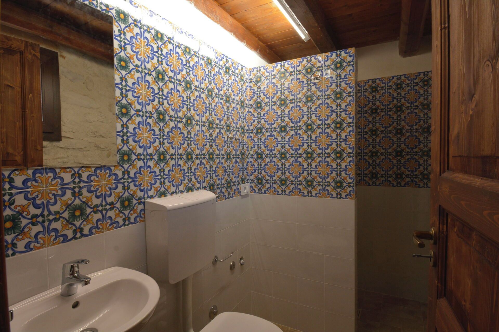 A bathroom with a sink, toilet, and shower area, featuring patterned tiles and wooden elements.