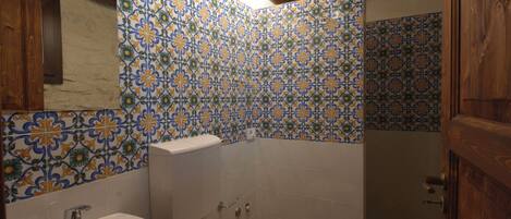 A bathroom with a sink, toilet, and shower area, featuring patterned tiles and wooden elements.