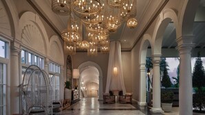 En rummelig lobby med højt til loftet, flere lysekroner og et centralt siddeområde med stole og sofa.