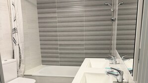 Ein modernes Badezimmer mit Toilette, Bidet, Badewanne und einem großen Spiegel.