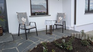 Eine Gebäudeecke mit zwei Stühlen, einem Tisch und einem Fenster mit Blumen.