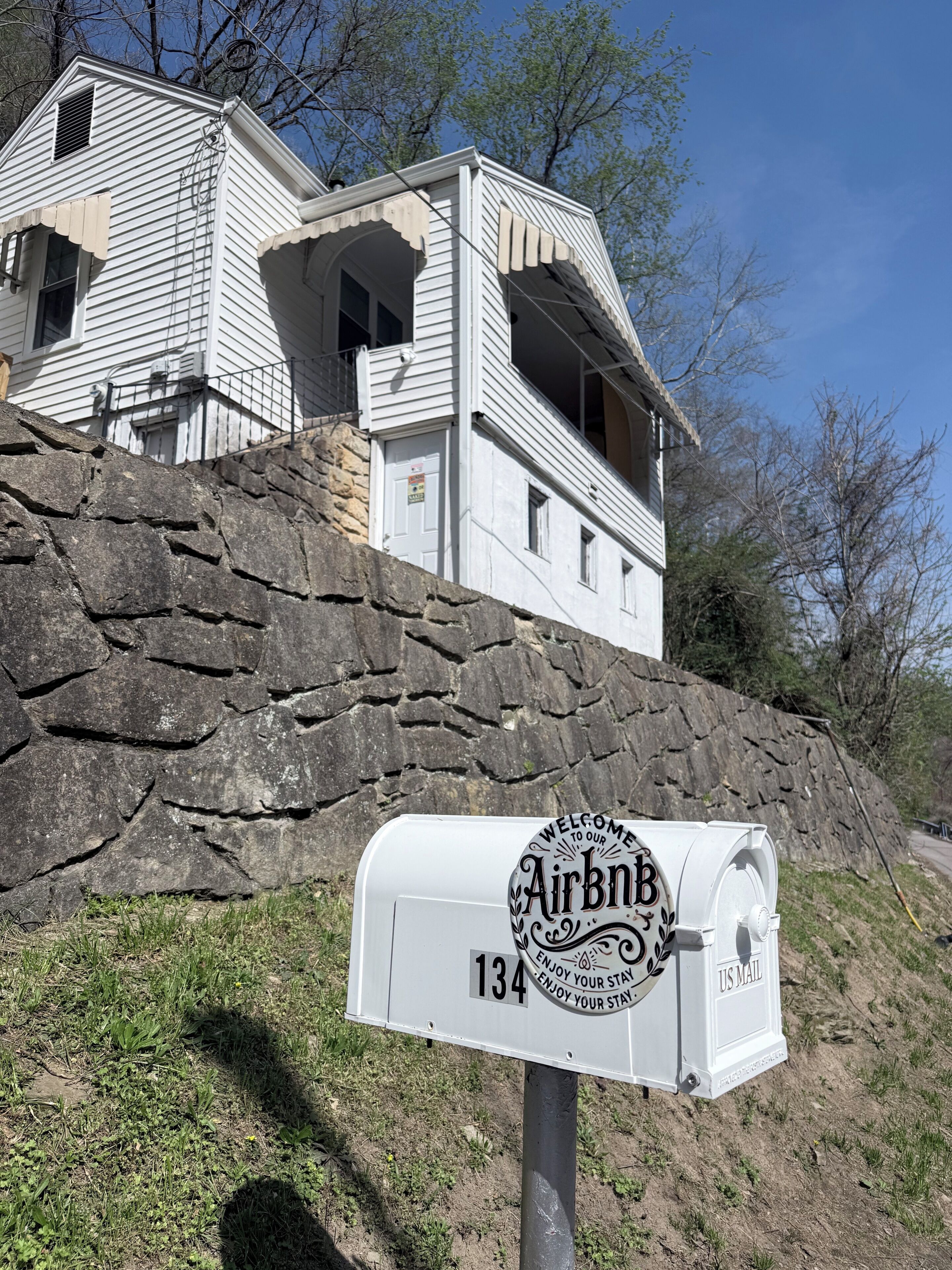 A white house with a stone wall, an Airbnb mailbox, and a clear sky.