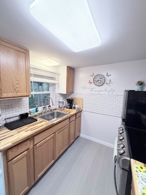 Une cuisine moderne avec des meubles en bois, une cuisinière noire, un évier et une fenêtre.