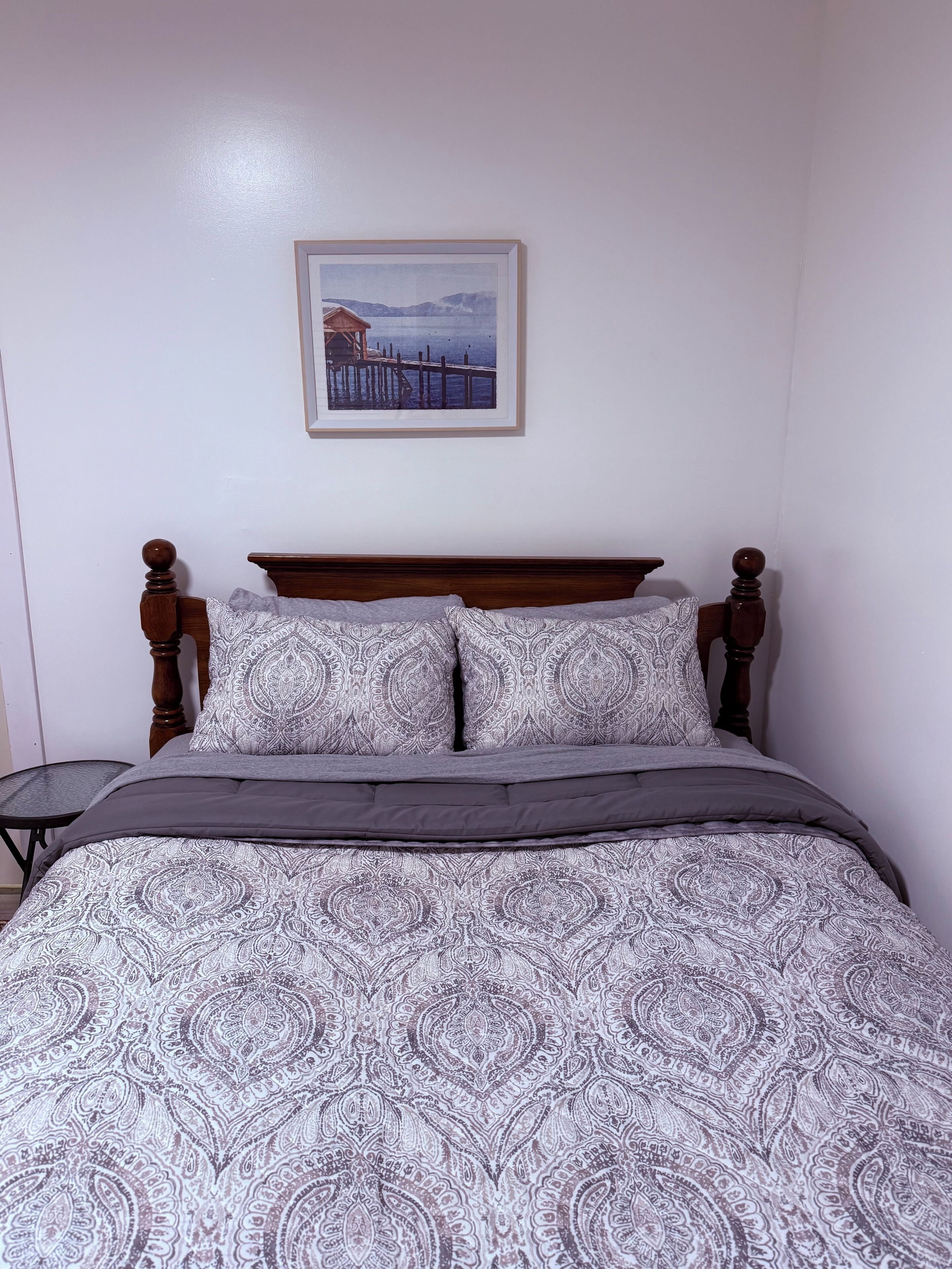 A bed with a patterned bedspread, a wooden headboard, and a framed picture on the wall.