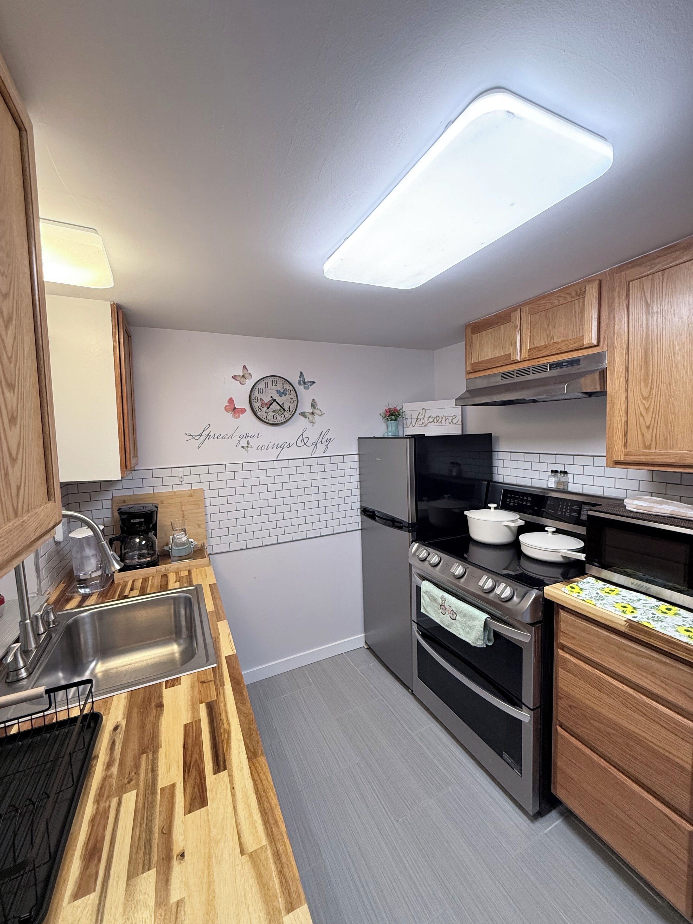 Una cocina con encimera de madera, electrodomésticos de acero inoxidable, un reloj de pared y un cartel con el lema 'Spread your wings & fly'.