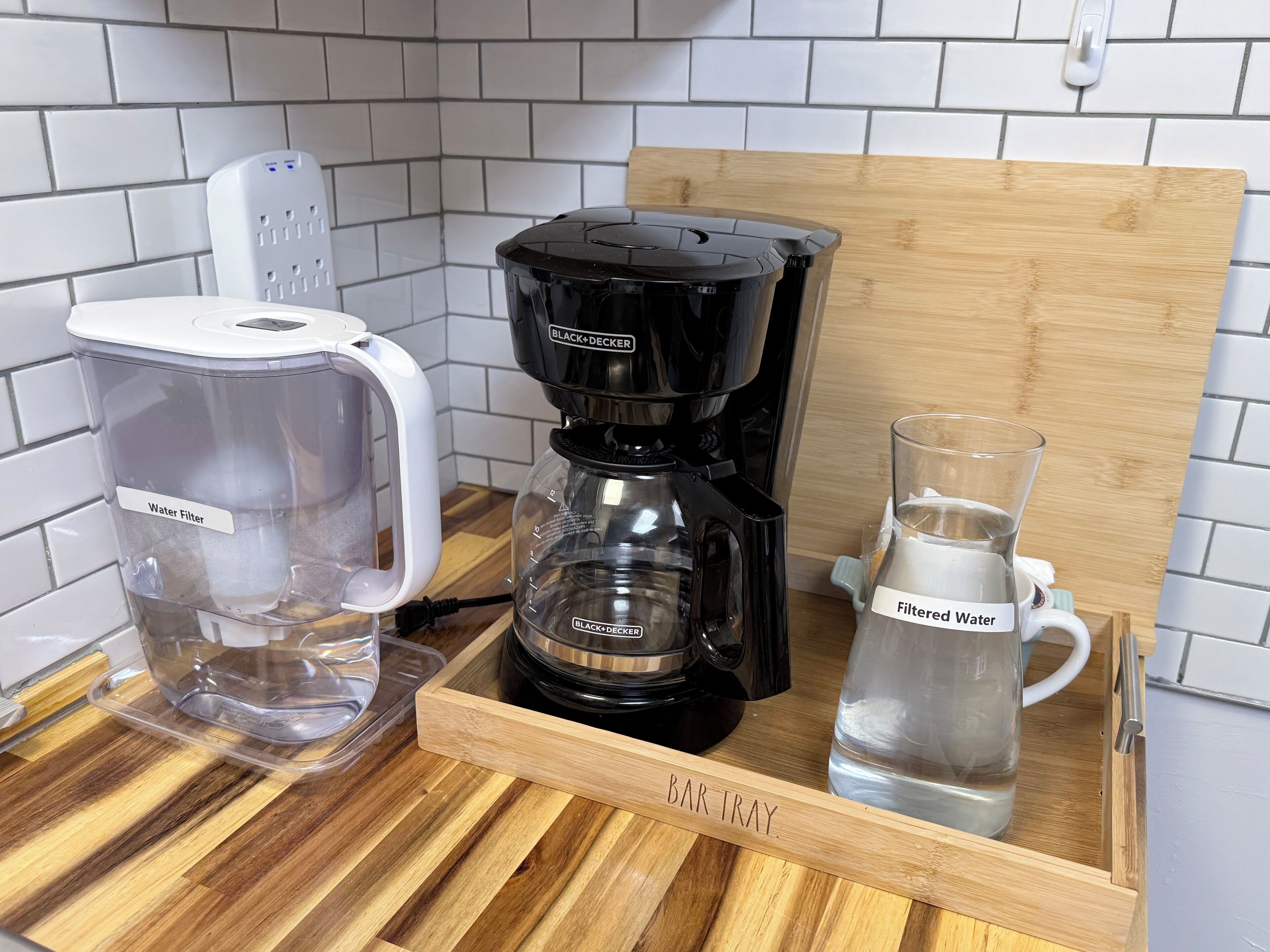 Un coin cuisine équipé d’un filtre à eau, d’une machine à café et d’une carafe d’eau portant l’étiquette « Eau filtrée », le tout placé sur un plateau en bois.