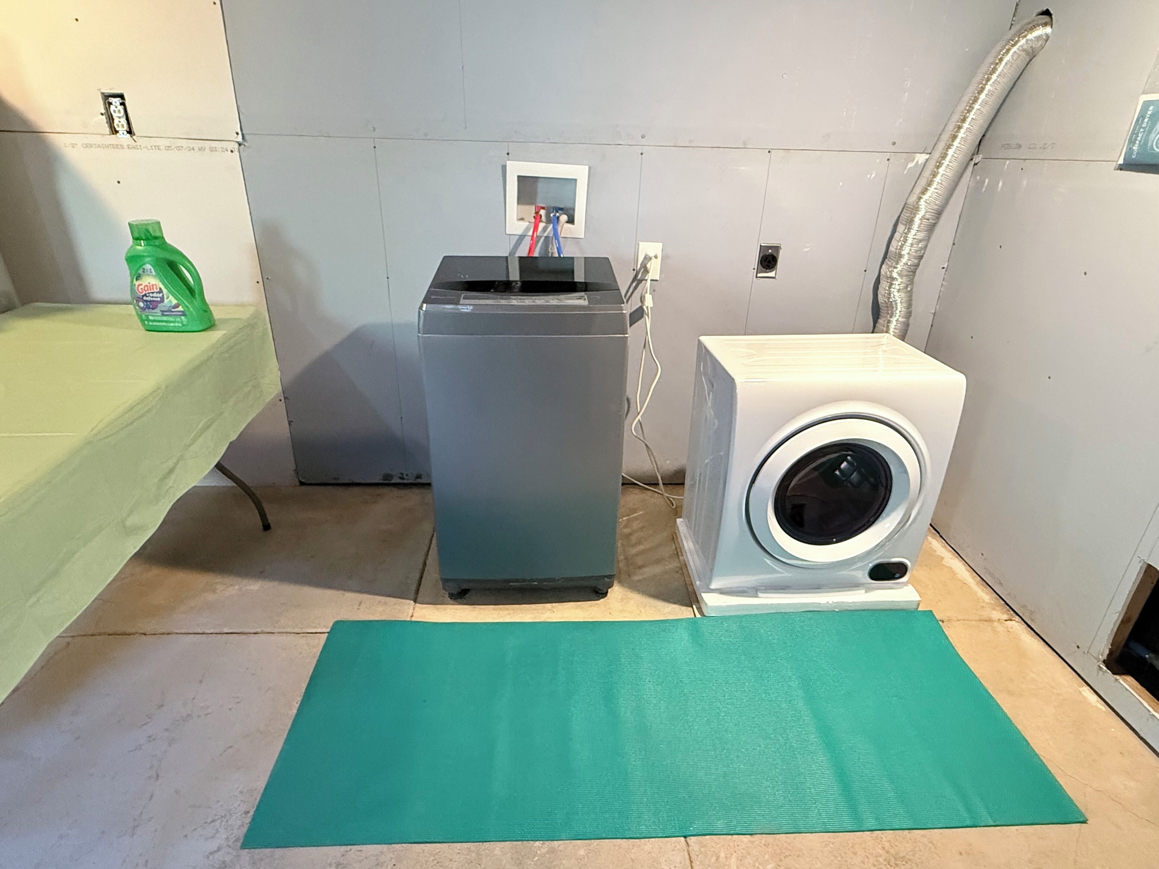 Uma lavanderia com máquina de lavar, secadora e um tapete verde no chão.