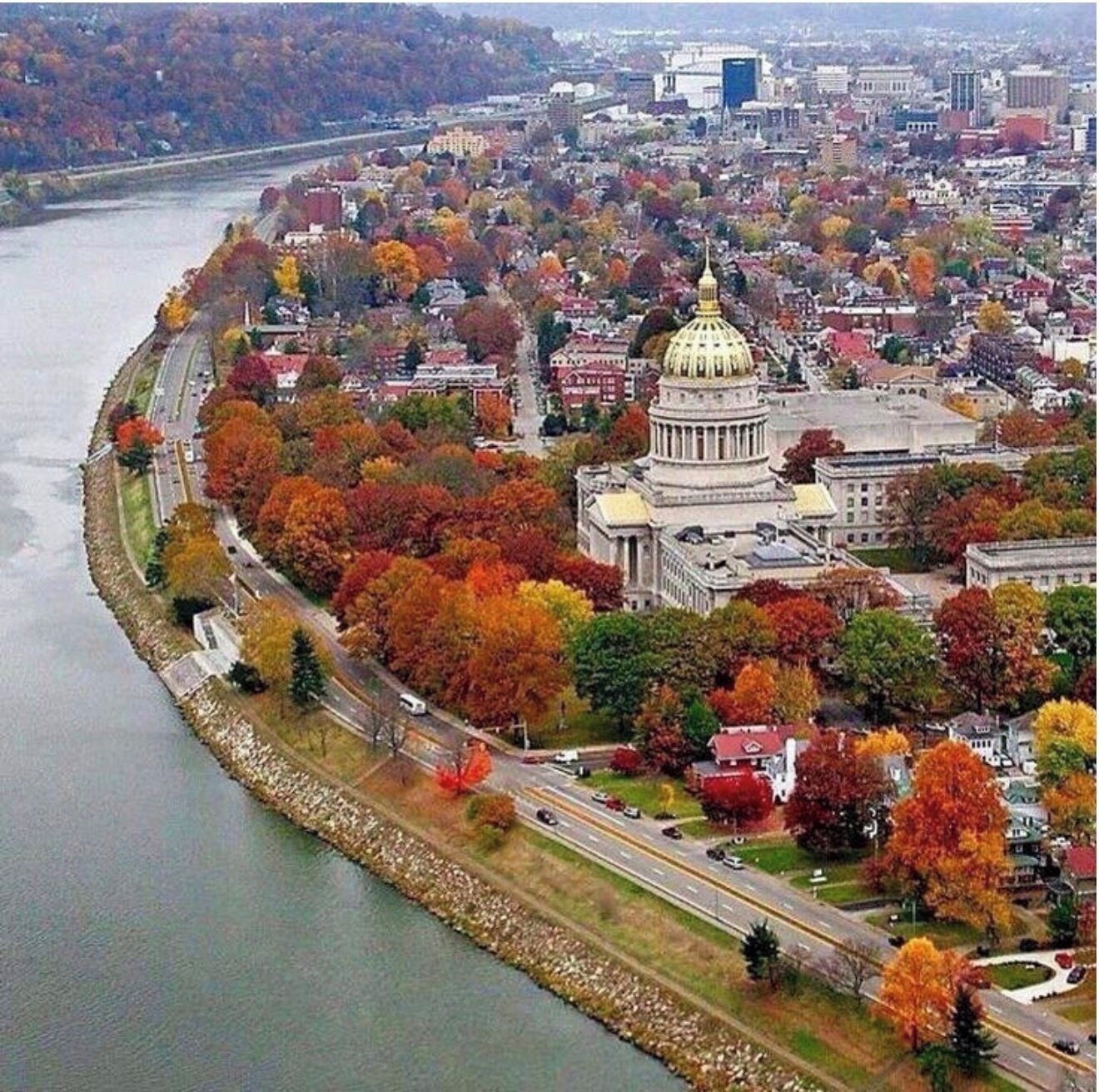 An aerial view of a city with a prominent government building, a river, and autumn foliage.