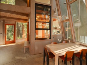 A modern interior with a wooden dining table, chairs, and large windows offering views of the surrounding forest. - Modern Forest Retreat on 2 Acres: Near Cape Meares Beach & Steam Shower (Tillamook)
