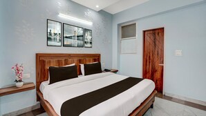 Una habitación de hotel con una cama grande, cabecera de madera, mesita de noche, lámpara de pared y una puerta.