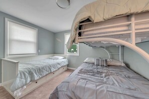 Ein Zimmer mit Etagenbetten, einem Fenster mit Jalousien, einem Heizkörper und einer kleinen grünen Pflanze.