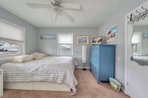 A bedroom with a bed, a dresser, a ceiling fan, and wall art.