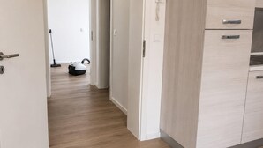 Käytävä, jossa on pölynimuri, ovi, jossa on puhelin, ja keittiöalue, jossa on kaappeja.