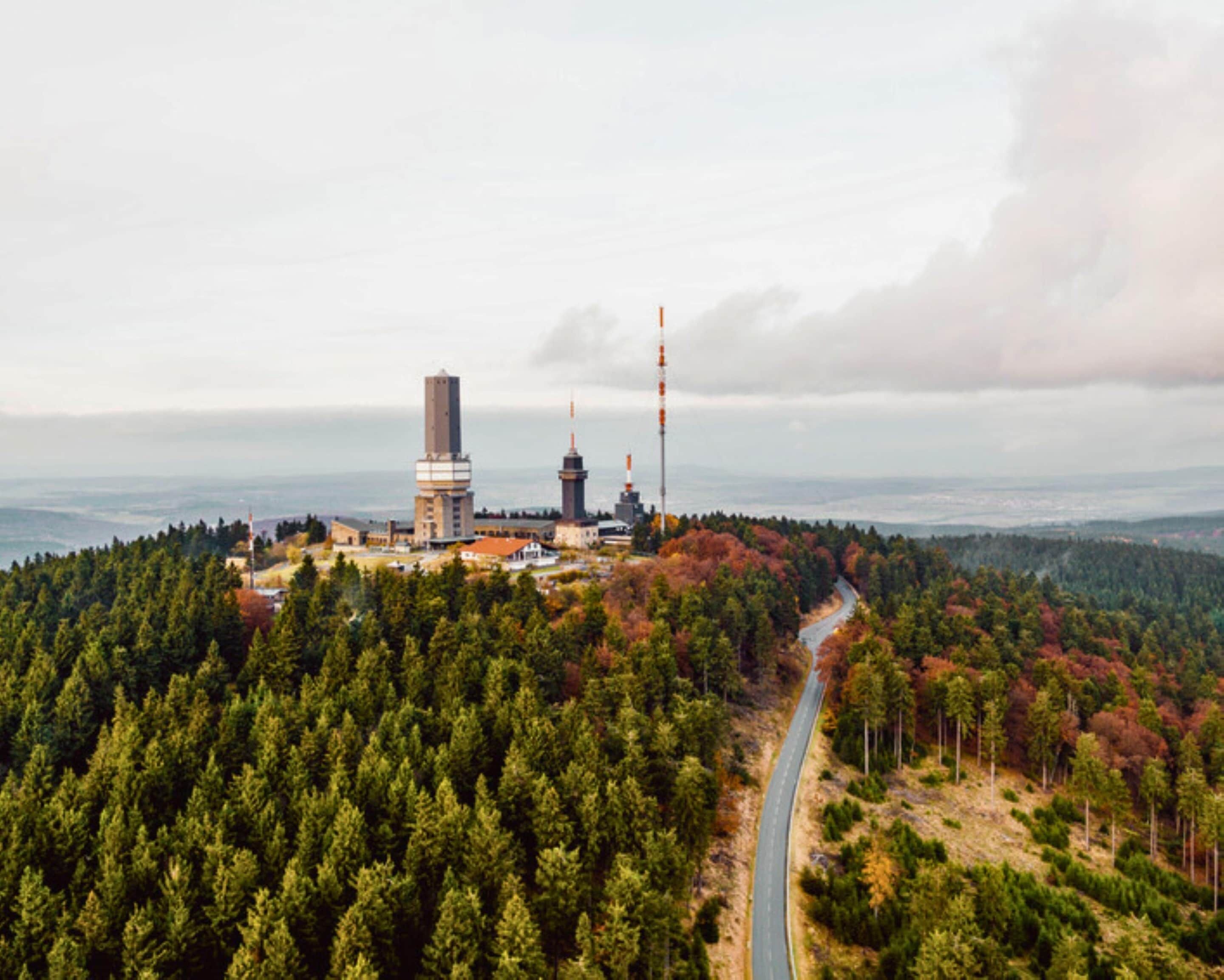 Un paisaje montañoso con una carretera, un bosque denso y varias estructuras altas, incluyendo una torre destacada.