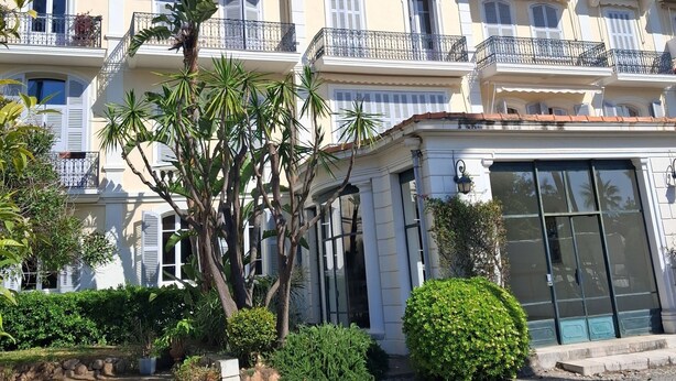 A multi-story building with balconies, a gated entrance, and a well-maintained garden. - Spacious, air-conditioned apartment in a lush, green setting, ideal for families. (Cannes)