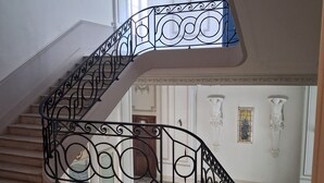 A grand staircase with ornate black metal railings, a tiled floor, and classical wall decorations. - Spacious, air-conditioned apartment in a lush, green setting, ideal for families. (Cannes)