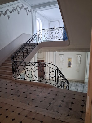 Eine prachtvolle Treppe mit aufwendigen schwarzen Metallgeländern, einem gefliesten Boden und klassischen Wandverzierungen.