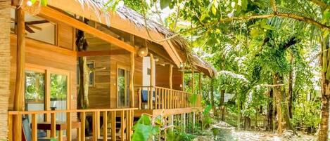 A wooden cabin with a balcony, surrounded by lush greenery.