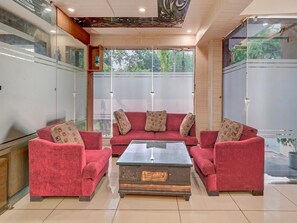 Ein modernes Wohnzimmer mit einer roten Sofagarnitur, einem Glastisch und großen Fenstern mit geätzten Glasscheiben.