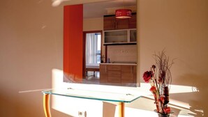 A modern interior with a glass-top table, a vase with flowers, and a kitchen area in the background. - Albania Dream Saranda Apartments (Sarandë)