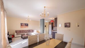 A dining area with a table, chairs, and a chandelier. There is a sofa and a kitchen in the background. - Albania Dream Saranda Apartments (Sarandë)