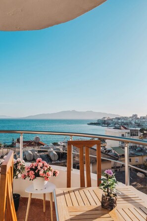 A balcony with a view of the sea, a wooden chair, a small table, and a potted plant. - Albania Dream Saranda Apartments (Sarandë)