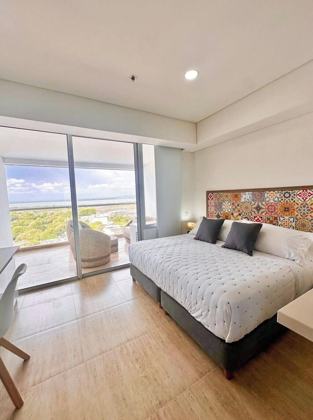 Une chambre moderne avec un grand lit, un bureau et une vue sur un paysage verdoyant, visible à travers une porte-fenêtre coulissante.