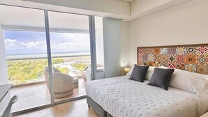 Un dormitorio moderno con una cama grande, un escritorio y vistas a un paisaje verde a través de un ventanal corredera.