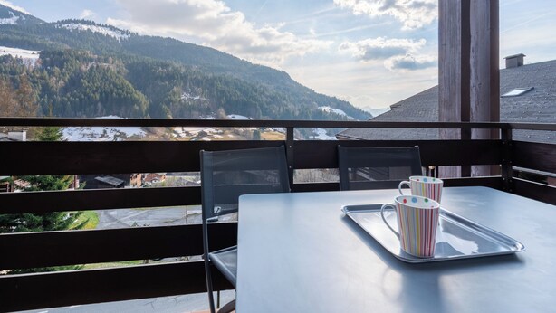Un balcon avec une table, deux tasses à rayures et un plateau.