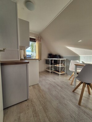 A compact kitchen with a refrigerator, a dining table with chairs, and a TV on a shelf.