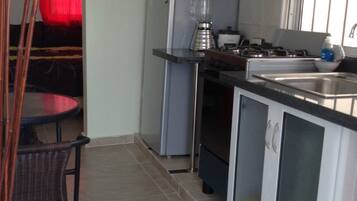 A compact kitchen with a refrigerator, stove, and a blender on the counter.